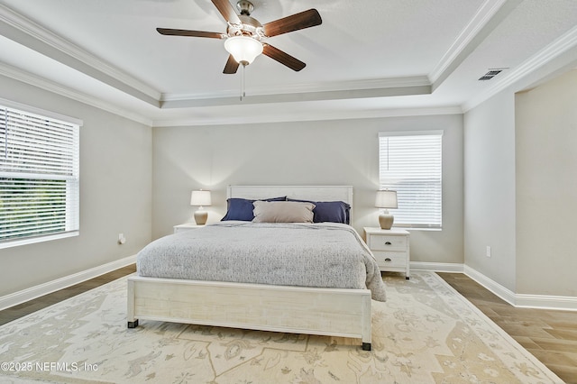 bedroom with ceiling fan, multiple windows, and a tray ceiling