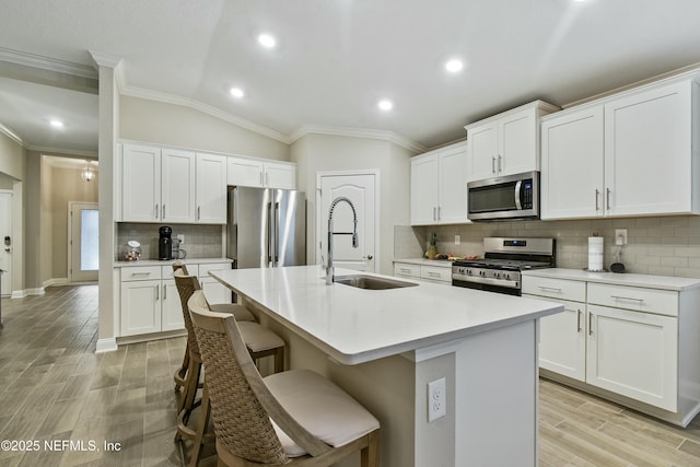 kitchen with vaulted ceiling, appliances with stainless steel finishes, white cabinetry, and a kitchen island with sink