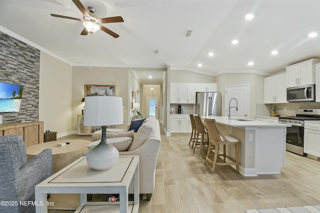 interior space with tasteful backsplash, lofted ceiling, sink, a kitchen island with sink, and appliances with stainless steel finishes