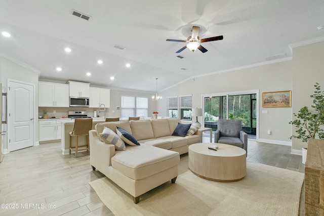 living room with lofted ceiling, crown molding, ceiling fan with notable chandelier, and sink