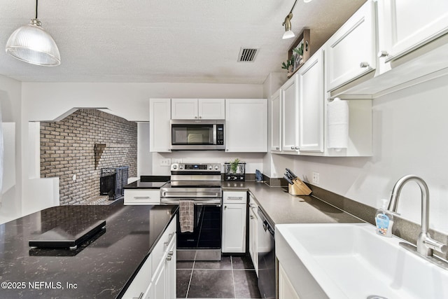 kitchen with sink, dark tile patterned flooring, pendant lighting, stainless steel appliances, and white cabinets