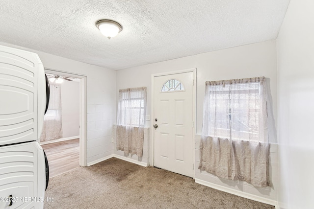 carpeted entryway featuring stacked washer and dryer and a textured ceiling