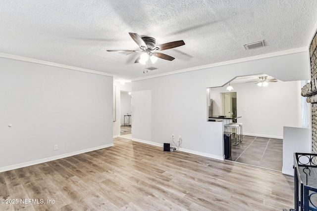 unfurnished room with a brick fireplace, a textured ceiling, ornamental molding, and ceiling fan