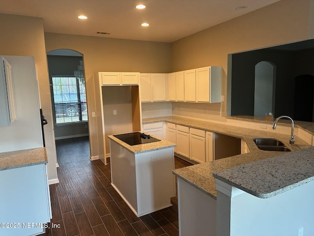 kitchen featuring sink, light stone countertops, white cabinets, a kitchen island, and kitchen peninsula