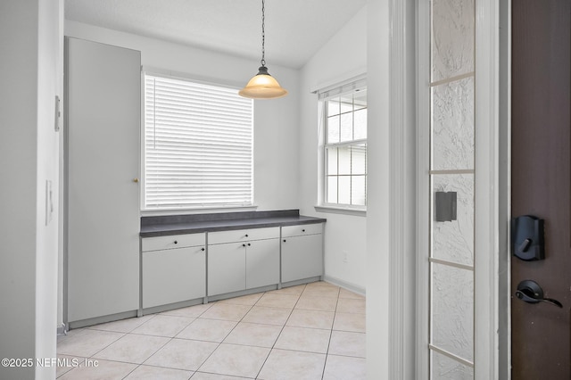 kitchen featuring white cabinetry, light tile patterned floors, lofted ceiling, and hanging light fixtures