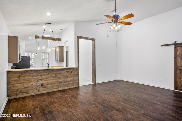 kitchen with black refrigerator, dark hardwood / wood-style flooring, kitchen peninsula, vaulted ceiling, and a barn door