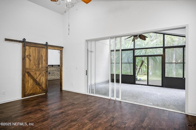 spare room featuring dark wood-type flooring, ceiling fan, a healthy amount of sunlight, and a barn door