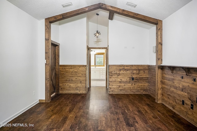 unfurnished room with a textured ceiling, dark hardwood / wood-style flooring, lofted ceiling with beams, and wooden walls