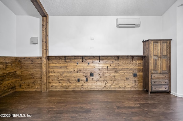 laundry area featuring dark wood-type flooring, wooden walls, a textured ceiling, and a wall mounted air conditioner