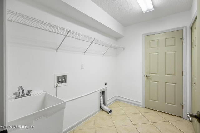 washroom with light tile patterned floors, hookup for an electric dryer, hookup for a washing machine, a textured ceiling, and sink