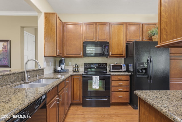 kitchen featuring sink, backsplash, black appliances, light stone countertops, and light wood-type flooring