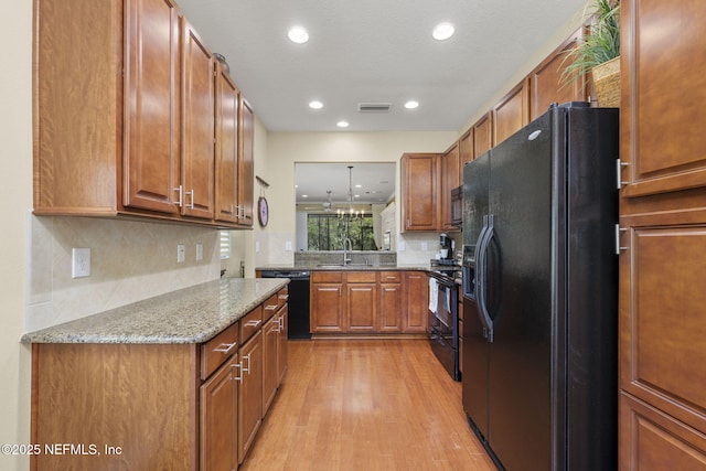 kitchen featuring decorative light fixtures, sink, light hardwood / wood-style floors, black appliances, and light stone countertops