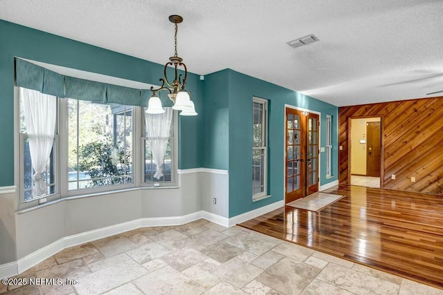 unfurnished dining area with a textured ceiling, wood walls, and a notable chandelier