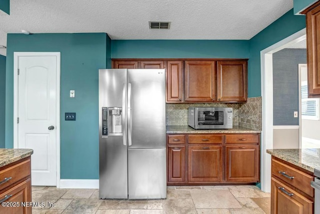 kitchen featuring backsplash, light stone countertops, a textured ceiling, and appliances with stainless steel finishes