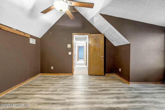 additional living space featuring light wood-type flooring, ceiling fan, lofted ceiling, and a textured ceiling