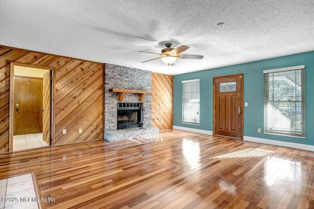 unfurnished living room with a brick fireplace, hardwood / wood-style flooring, wood walls, and ceiling fan