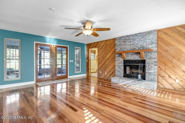 unfurnished living room featuring french doors, a brick fireplace, a wealth of natural light, and wooden walls