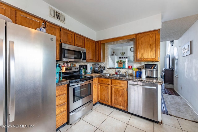 kitchen with light tile patterned flooring, appliances with stainless steel finishes, tasteful backsplash, sink, and dark stone counters