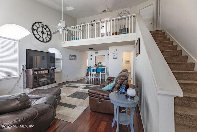 living room featuring a towering ceiling, a fireplace, dark hardwood / wood-style flooring, ceiling fan, and a textured ceiling