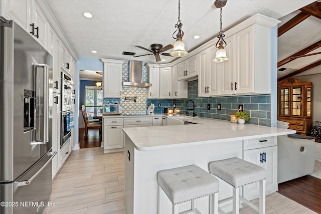 kitchen featuring appliances with stainless steel finishes, white cabinets, a kitchen bar, kitchen peninsula, and wall chimney exhaust hood