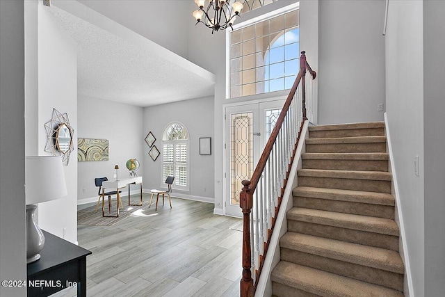 foyer entrance featuring a high ceiling, a textured ceiling, french doors, a chandelier, and light hardwood / wood-style flooring