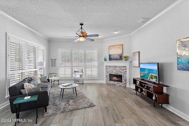 living room with ceiling fan, light hardwood / wood-style floors, crown molding, and a stone fireplace