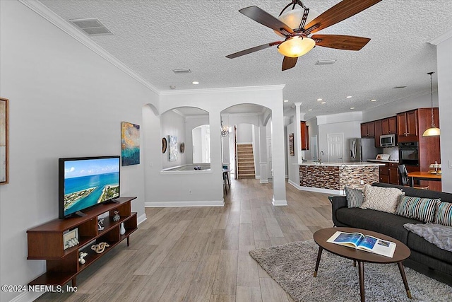 living room featuring ceiling fan, crown molding, a textured ceiling, and light hardwood / wood-style flooring