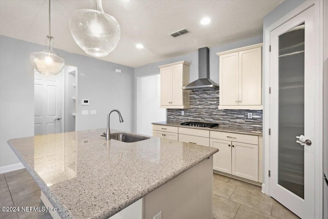 kitchen featuring sink, wall chimney exhaust hood, pendant lighting, and a kitchen island with sink