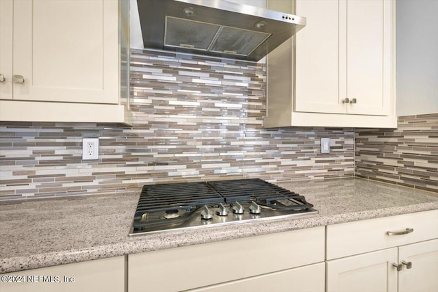 kitchen with ventilation hood, tasteful backsplash, stainless steel gas cooktop, white cabinets, and light stone counters