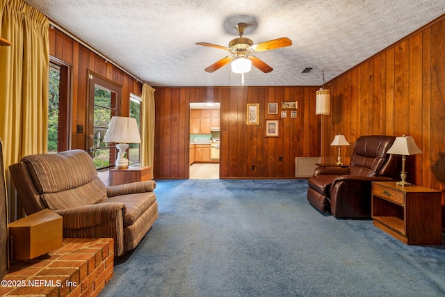 sitting room featuring carpet floors, a textured ceiling, ceiling fan, and wooden walls