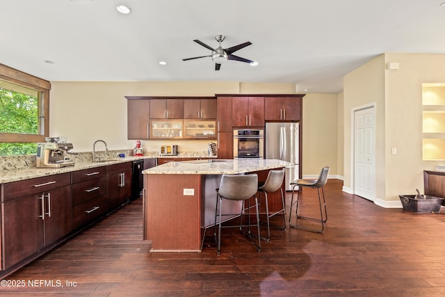 kitchen featuring a breakfast bar area, a center island, light stone counters, black appliances, and dark wood-type flooring