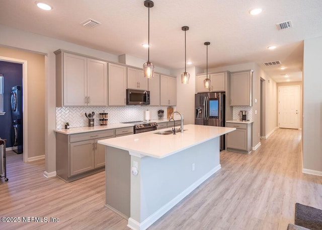 kitchen featuring sink, appliances with stainless steel finishes, a kitchen island with sink, decorative light fixtures, and light wood-type flooring