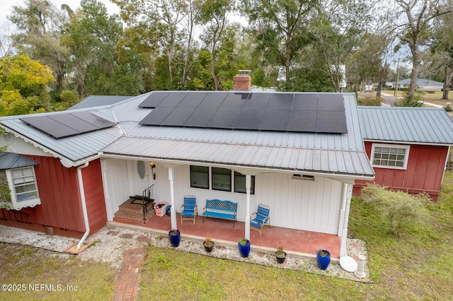 back of property with a yard, solar panels, and covered porch