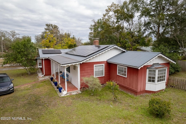 back of house featuring covered porch, a lawn, and solar panels