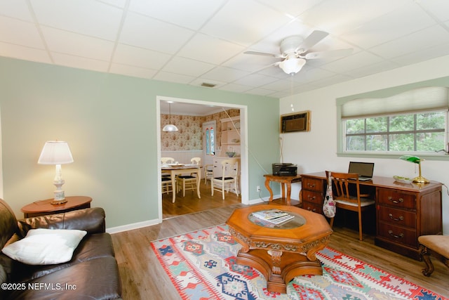 living room featuring light wood-type flooring, a paneled ceiling, ceiling fan, and a wall unit AC