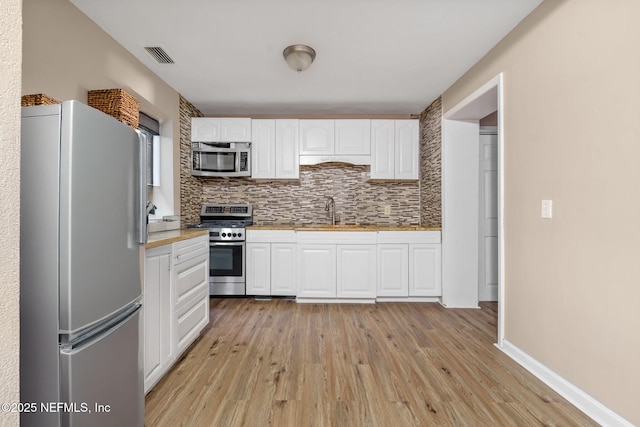 kitchen featuring tasteful backsplash, light hardwood / wood-style floors, white cabinets, and appliances with stainless steel finishes