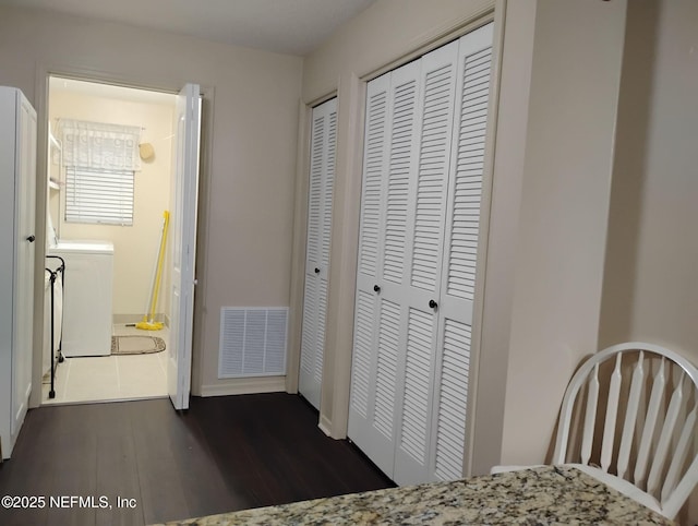 bedroom featuring washer / clothes dryer, dark wood-type flooring, and multiple closets