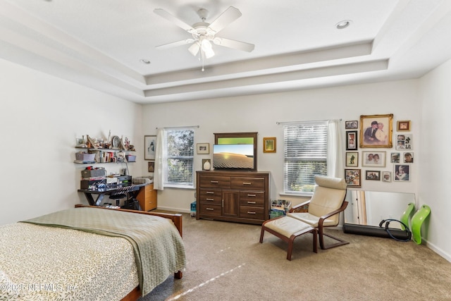 carpeted bedroom with a raised ceiling and ceiling fan