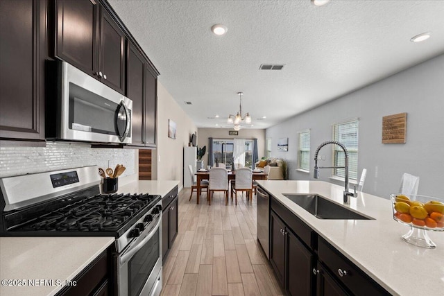 kitchen with appliances with stainless steel finishes, sink, light wood-type flooring, pendant lighting, and backsplash