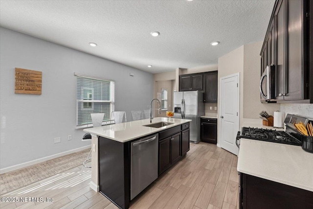 kitchen featuring a textured ceiling, appliances with stainless steel finishes, light hardwood / wood-style floors, sink, and a kitchen island with sink