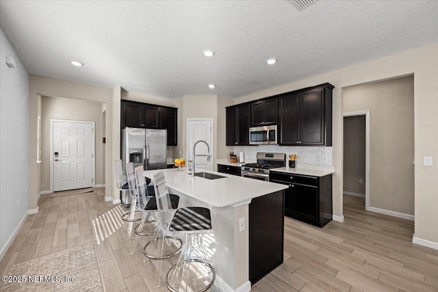 kitchen with appliances with stainless steel finishes, an island with sink, light hardwood / wood-style floors, sink, and a breakfast bar