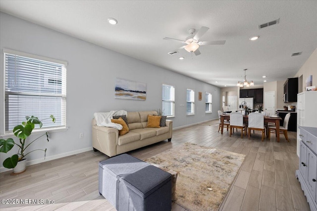 living room with a textured ceiling, light wood-type flooring, and ceiling fan with notable chandelier