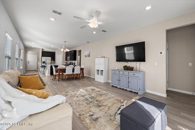 living room with ceiling fan with notable chandelier and light hardwood / wood-style floors