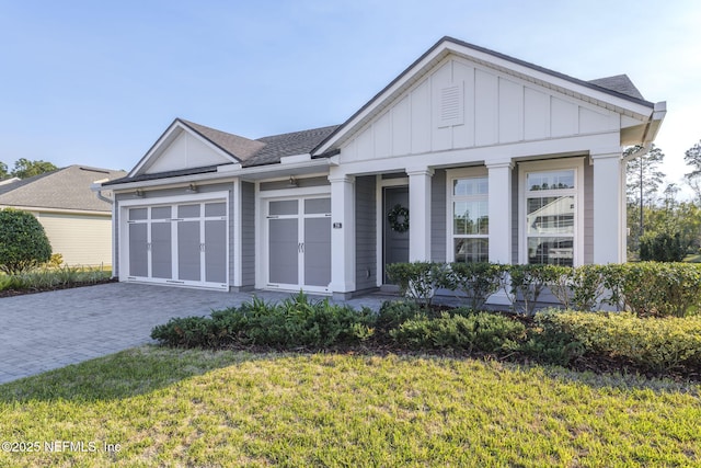 view of front of property featuring a garage, decorative driveway, a front lawn, and board and batten siding