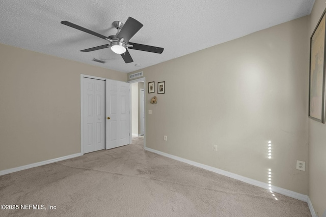 unfurnished bedroom with a textured ceiling, ceiling fan, a closet, and light colored carpet