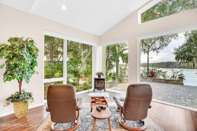 sunroom featuring a water view, vaulted ceiling, and a wood stove