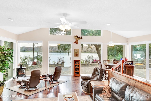 sunroom with ceiling fan, a wood stove, a water view, and vaulted ceiling