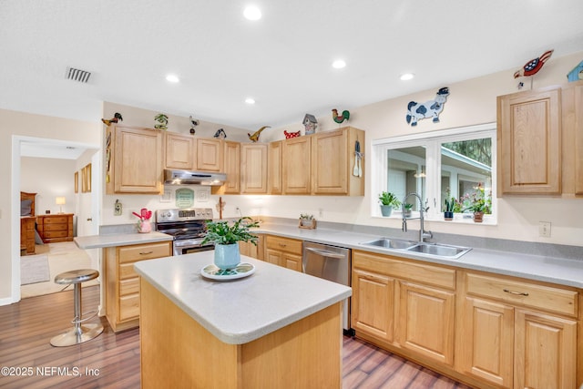 kitchen with appliances with stainless steel finishes, light brown cabinets, a kitchen island, light hardwood / wood-style flooring, and sink