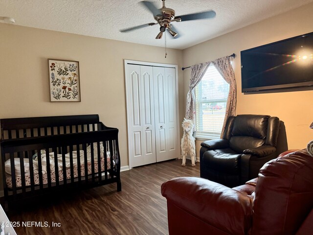 bedroom with dark hardwood / wood-style floors, ceiling fan, a crib, a textured ceiling, and a closet