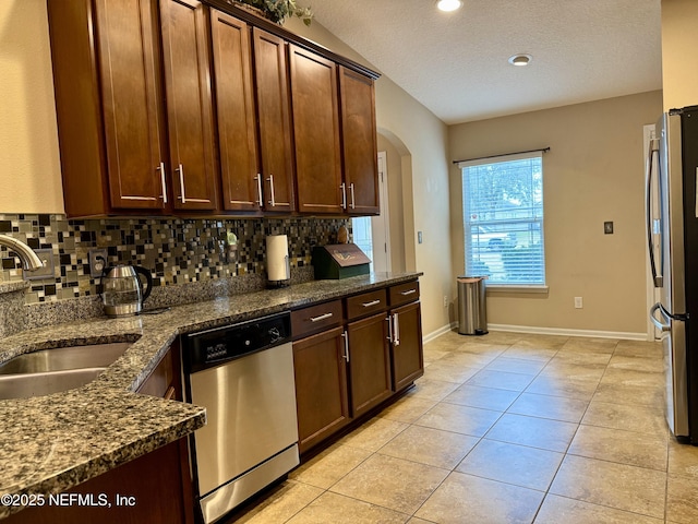 kitchen with lofted ceiling, backsplash, stainless steel appliances, and dark stone counters